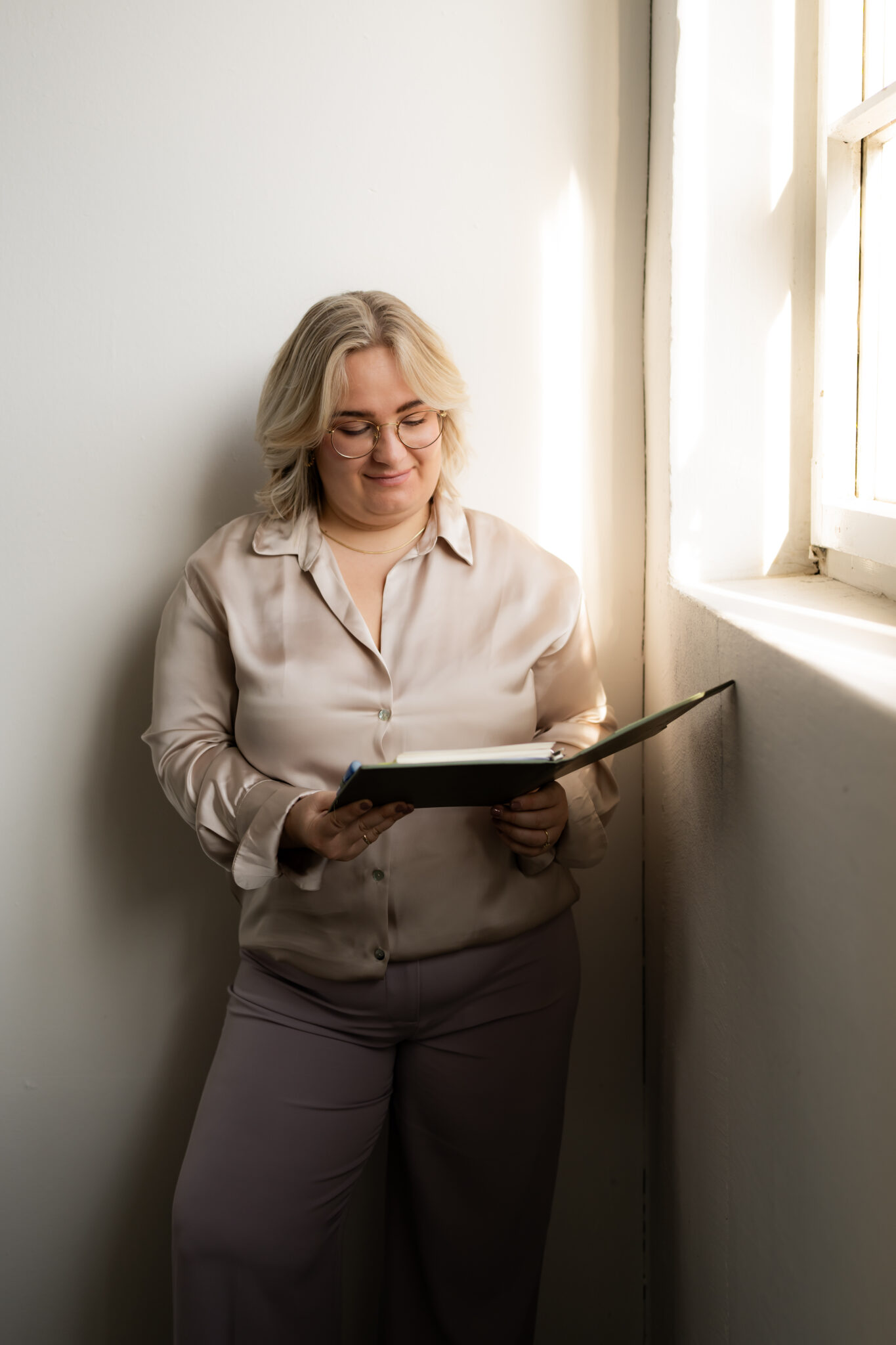 Katharina Heimberger am Fenster. Sie hält ein Notizbuch. Bild für Kontaktaufnahme. Nachhaltige Finanzberatung Landshut und Umgebung.